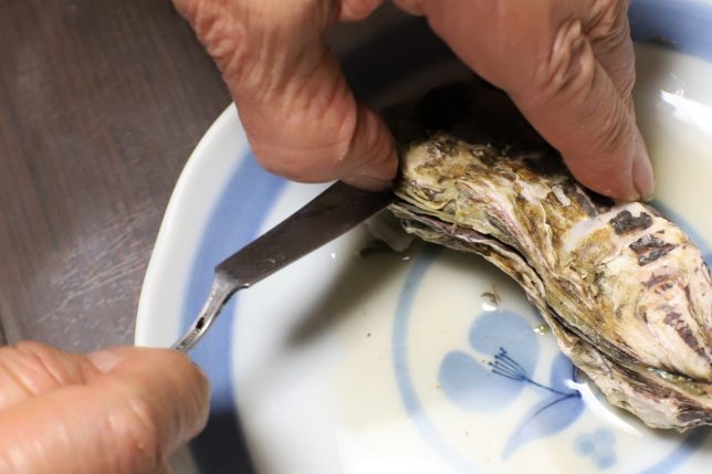 バターナイフを殻の間に差し込んで、蒸し牡蠣を開けるところ