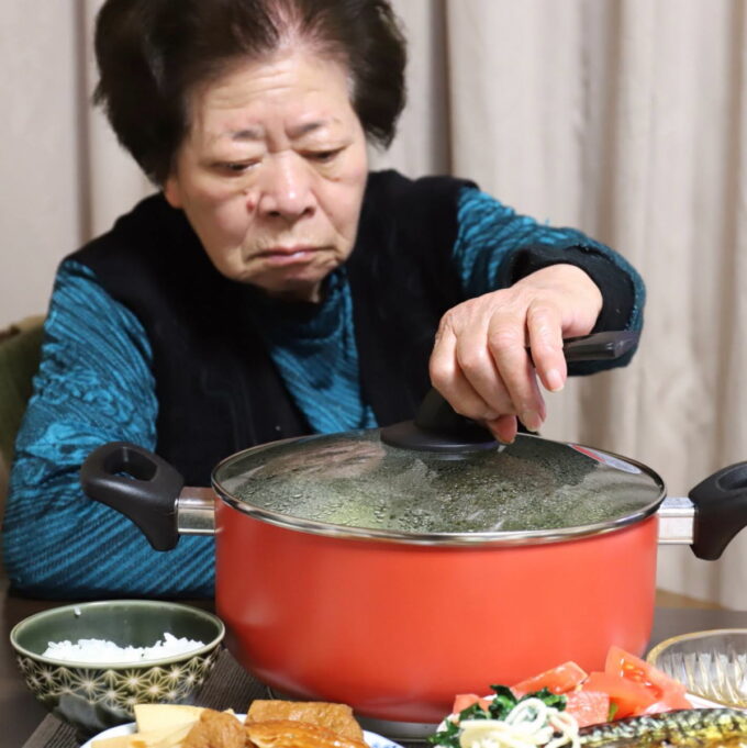 食卓で鍋のフタを取ろうとする祖母（おばあ）
