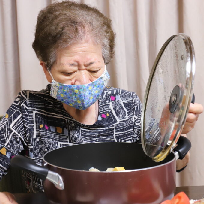 食卓に置いた鍋のフタを開ける祖母（おばあ）