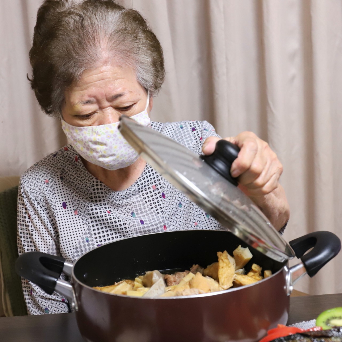 食卓で鍋のフタを開けている祖母・おばあ