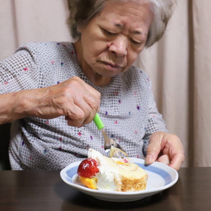 皿に切り分けたロールケーキを食べる祖母