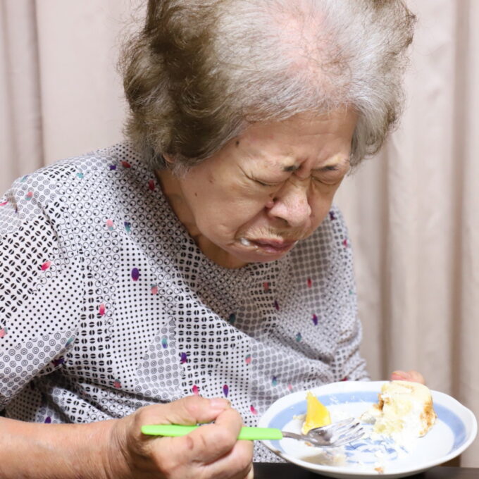 ケーキのトッピングのオレンジを食べて顔をしかめる祖母