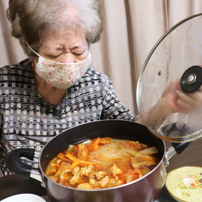鍋の蓋を開ける祖母とキムチ鍋