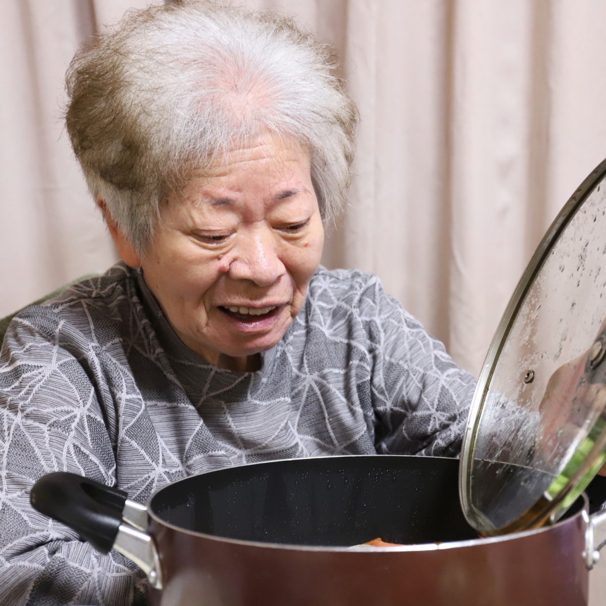 鍋のフタを持ち上げて笑顔を見せる祖母・おばあ