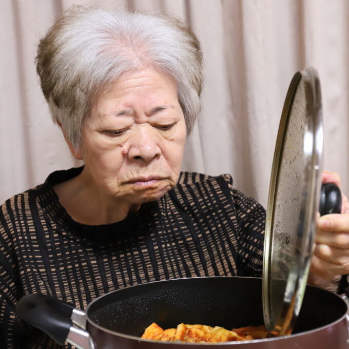 食卓に着いて鍋のフタを開ける祖母・おばあ