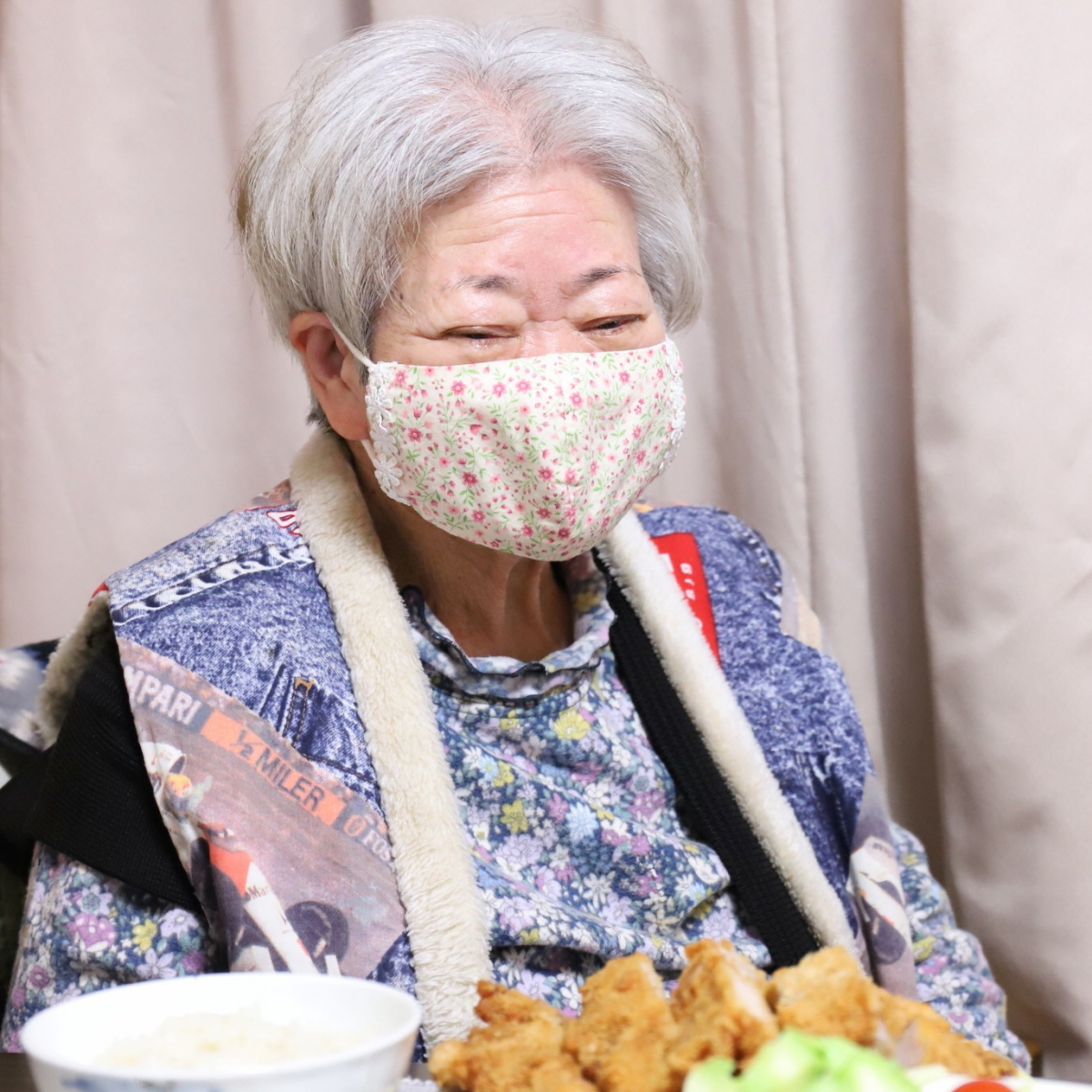 食卓に座ってマスクを着けて笑顔の祖母