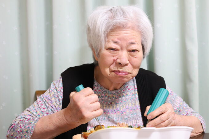 介護用スプーンで食事をして笑顔を見せる高齢の祖母