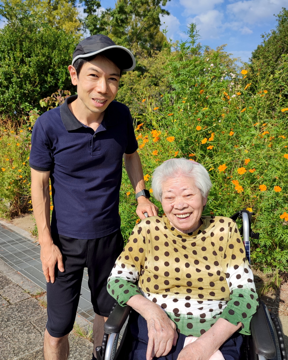 公園の花の前で笑顔の車椅子に乗った祖母と孫