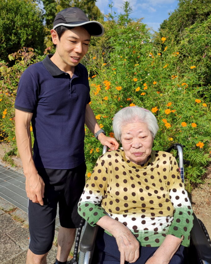 公園の花の前に映る車椅子に乗った祖母と孫