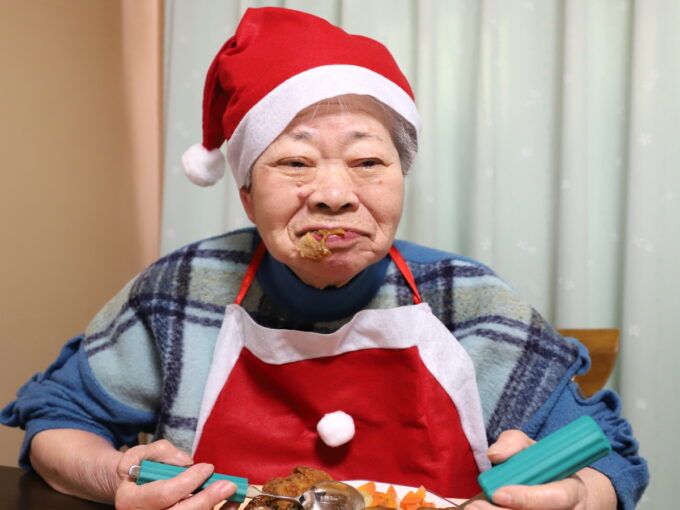 クリスマスのチキンを口に運んで笑顔の祖母（おばあ）