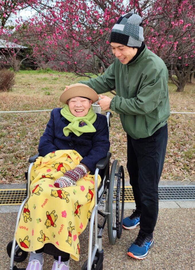梅の花の前にいる車椅子に乗った祖母と孫