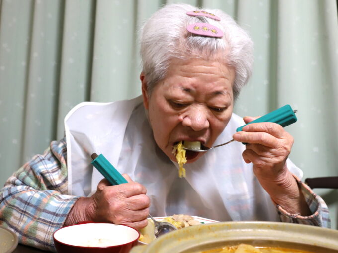 介護用スプーンを使って鍋の具材を食べる祖母