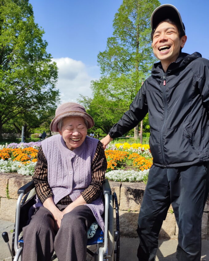 青空と緑と花を背景に笑う祖母と孫