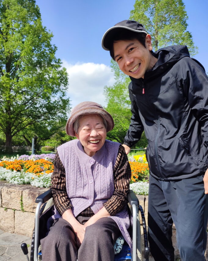 青空と花と緑がある公園で撮ったおばあちゃんと孫のツーショット写真