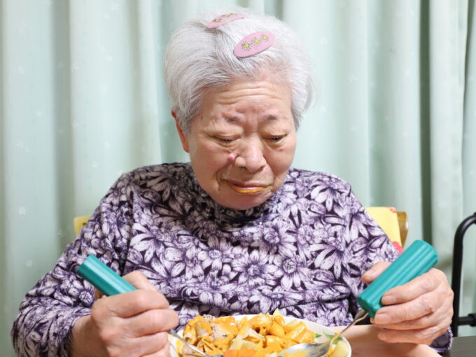 介護用スプーンで食事をして笑いをこらえている祖母