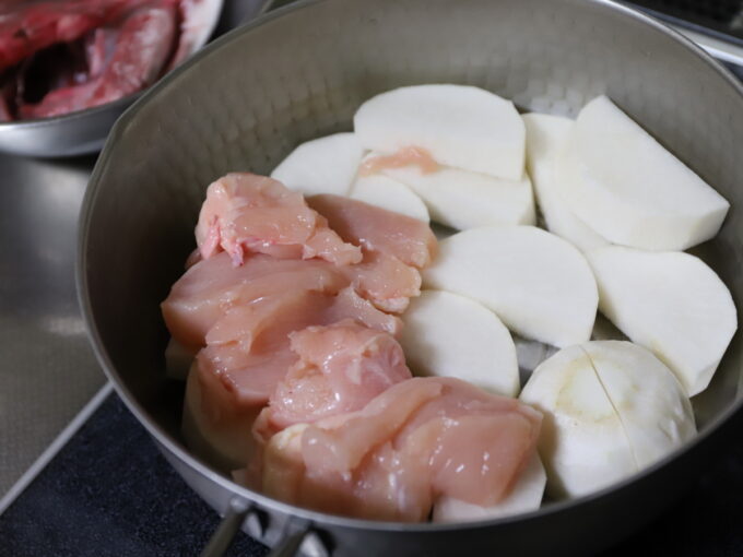 ステンレスの鍋に入れた、煮物にする前の半月切りにした大根と鶏肉