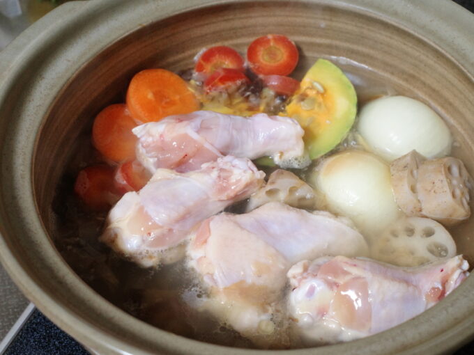 鶏肉や根菜を入れて土鍋で調理しているところ