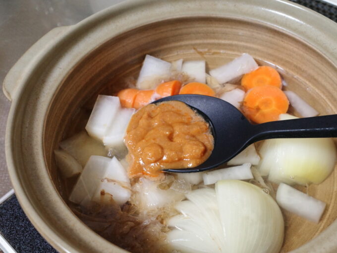 土鍋で具材を煮込み、まつやピリ辛とり野菜みそをお玉に入れて、味付けしている