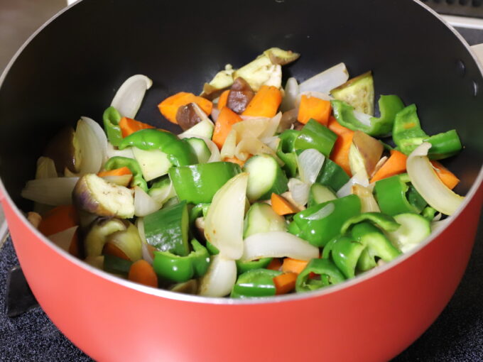 鍋で炒めて料理している、ピーマンやニンジンや玉ねぎなどの野菜