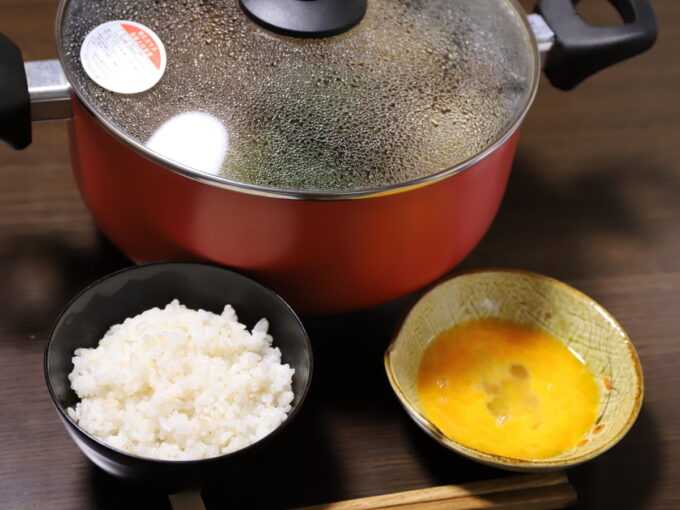 フタをしたすき焼きが入った鍋とごはんが入った茶碗と生卵が入った器を食卓に並んでいる。