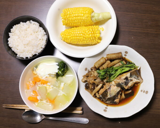 真上から撮った食卓に並べた夕飯。ごはん、カレイの煮つけや野菜スープ、とうもろこし