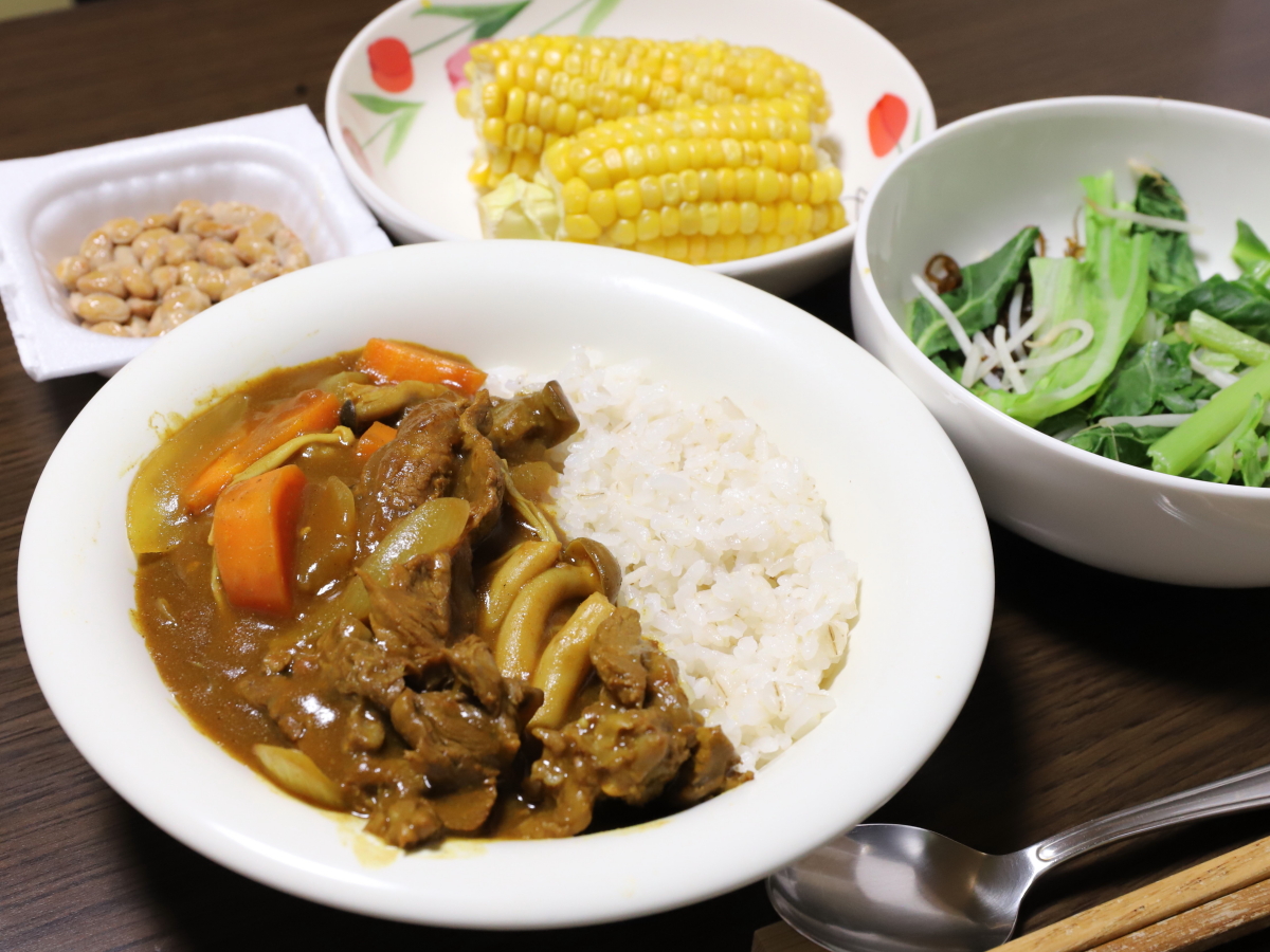 皿に盛り付けたカレーやサラダ、納豆など、食卓に並べた晩ごはんの献立