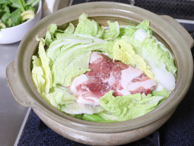 土鍋に白菜や豚肉を入れて煮て、鍋料理を作っているところ