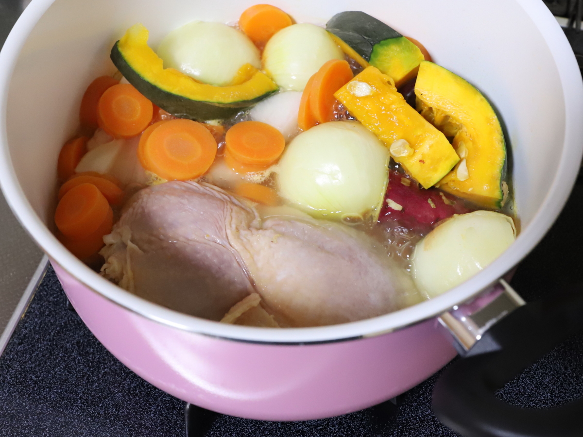 鍋で煮込んでいるカボチャやニンジンや玉ねぎ、鶏肉などの料理の食材