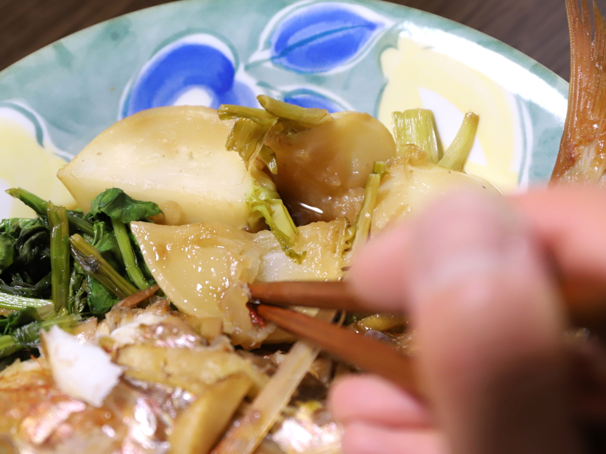 皿に盛りつけたカブの煮つけを箸を使って食べている