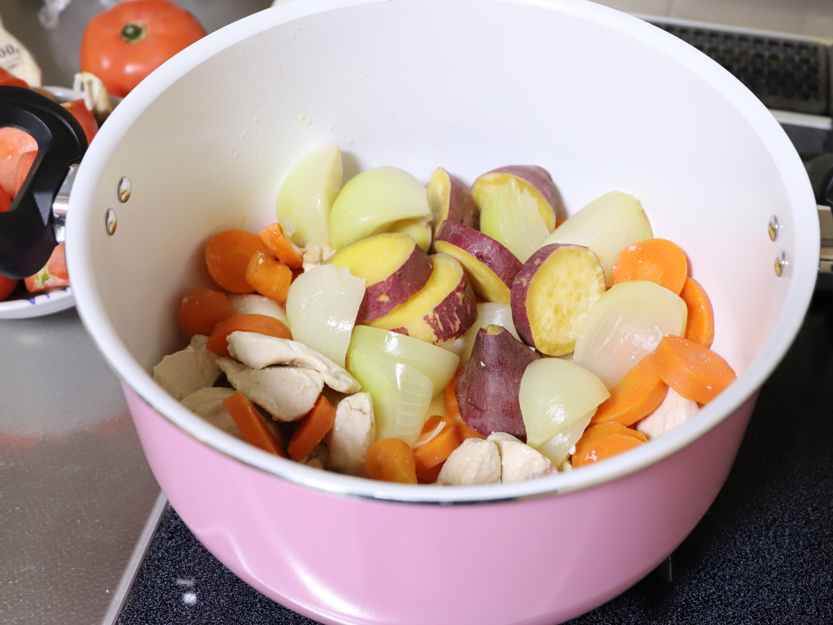 鍋でニンジンや玉ねぎなどを炒めてクリームシチューを作っている