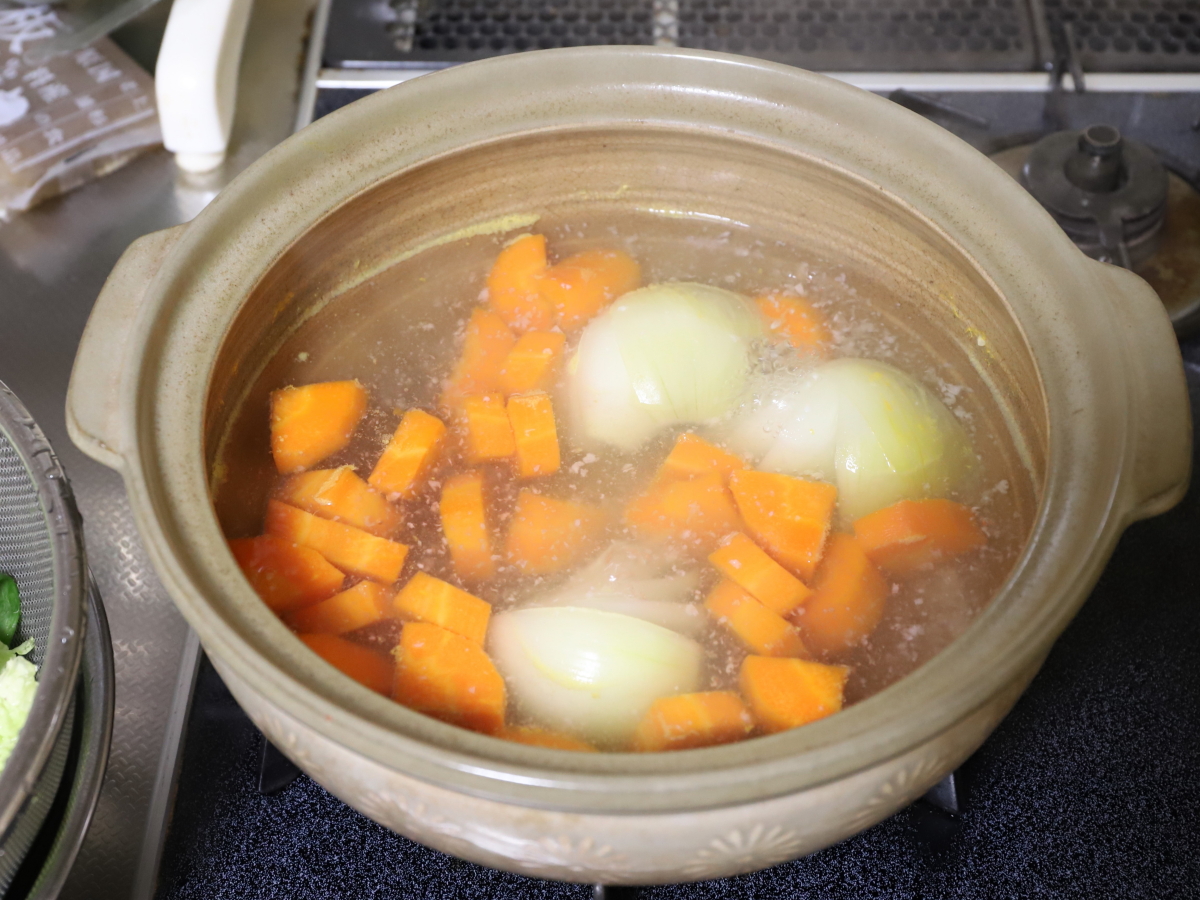土鍋でニンジンと玉ねぎを煮ている。