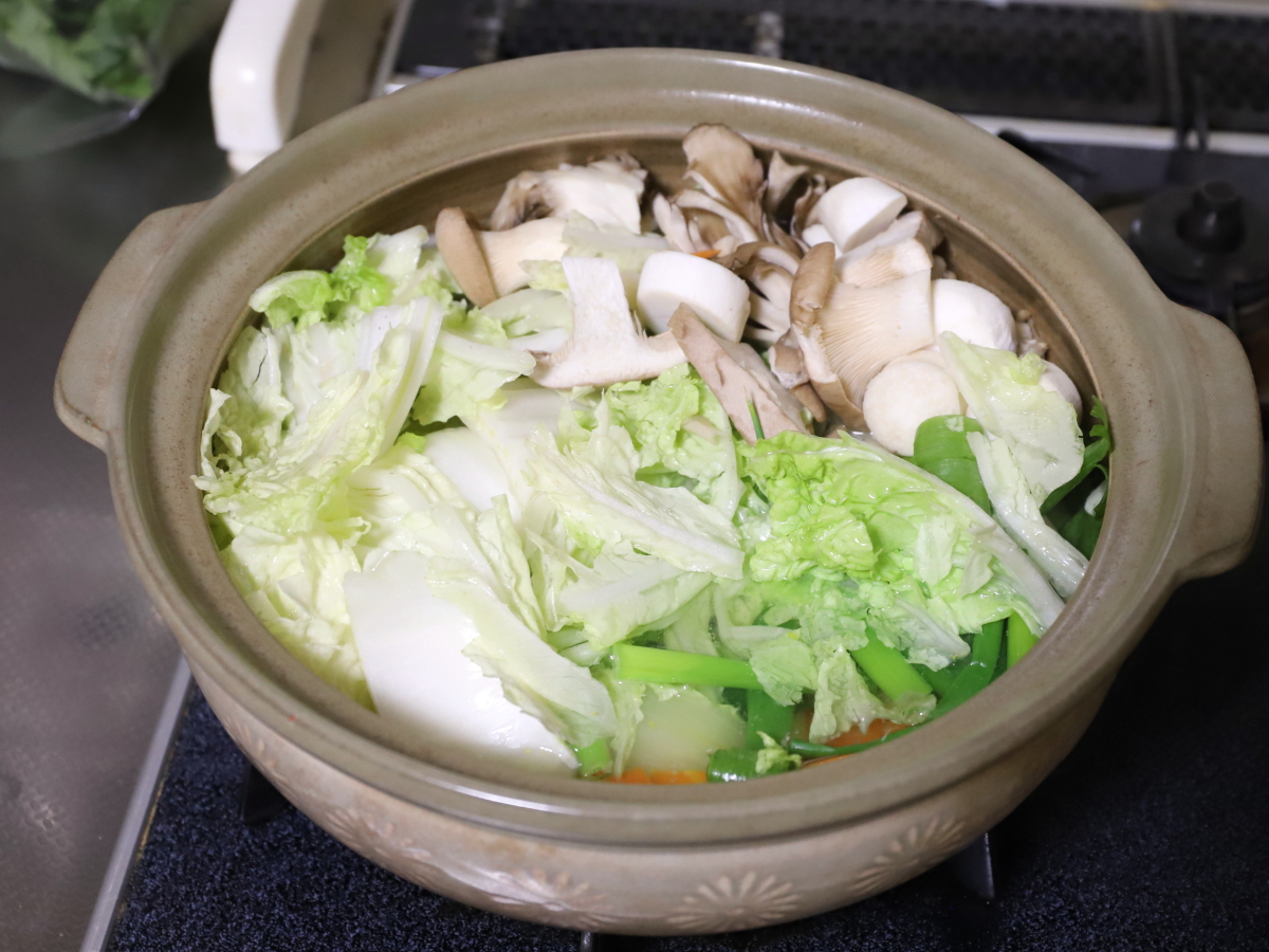 土鍋に白菜やネギ、キノコなどを入れて鍋料理を作っているところ