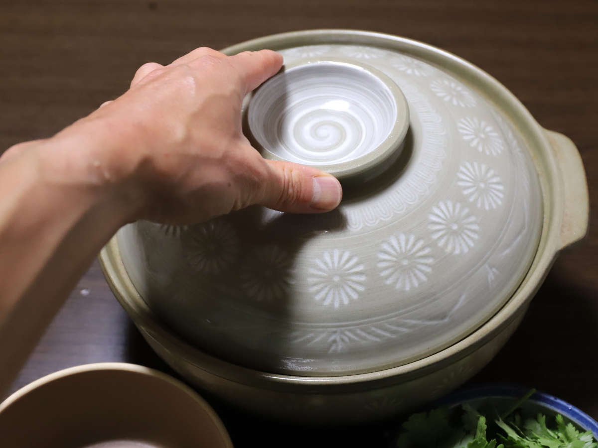 土鍋のフタを片手でつかんで、フタを開けようとしている